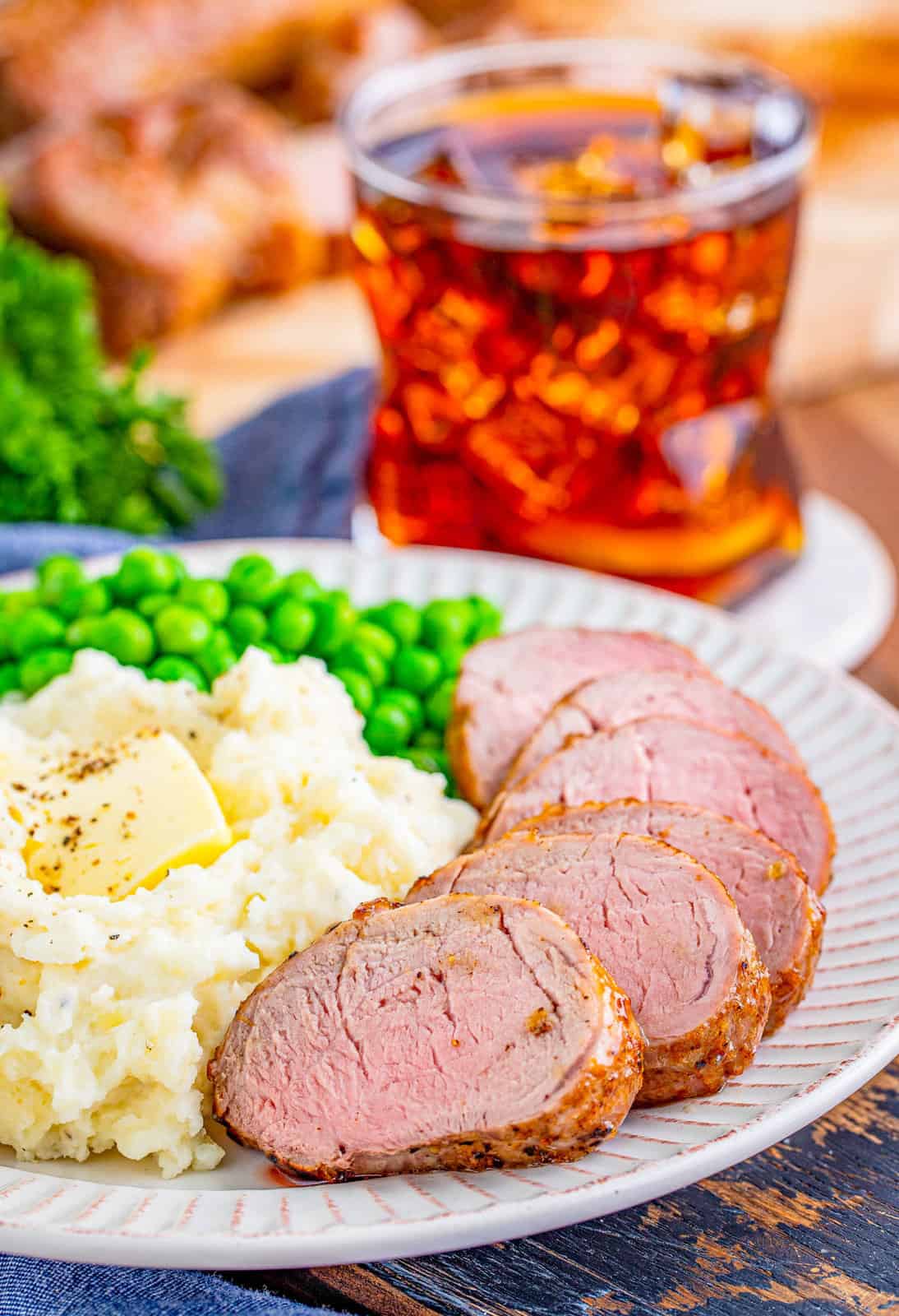 Sliced up Maple Dijon Pork Tenderloin on white plate with potatoes and peas.