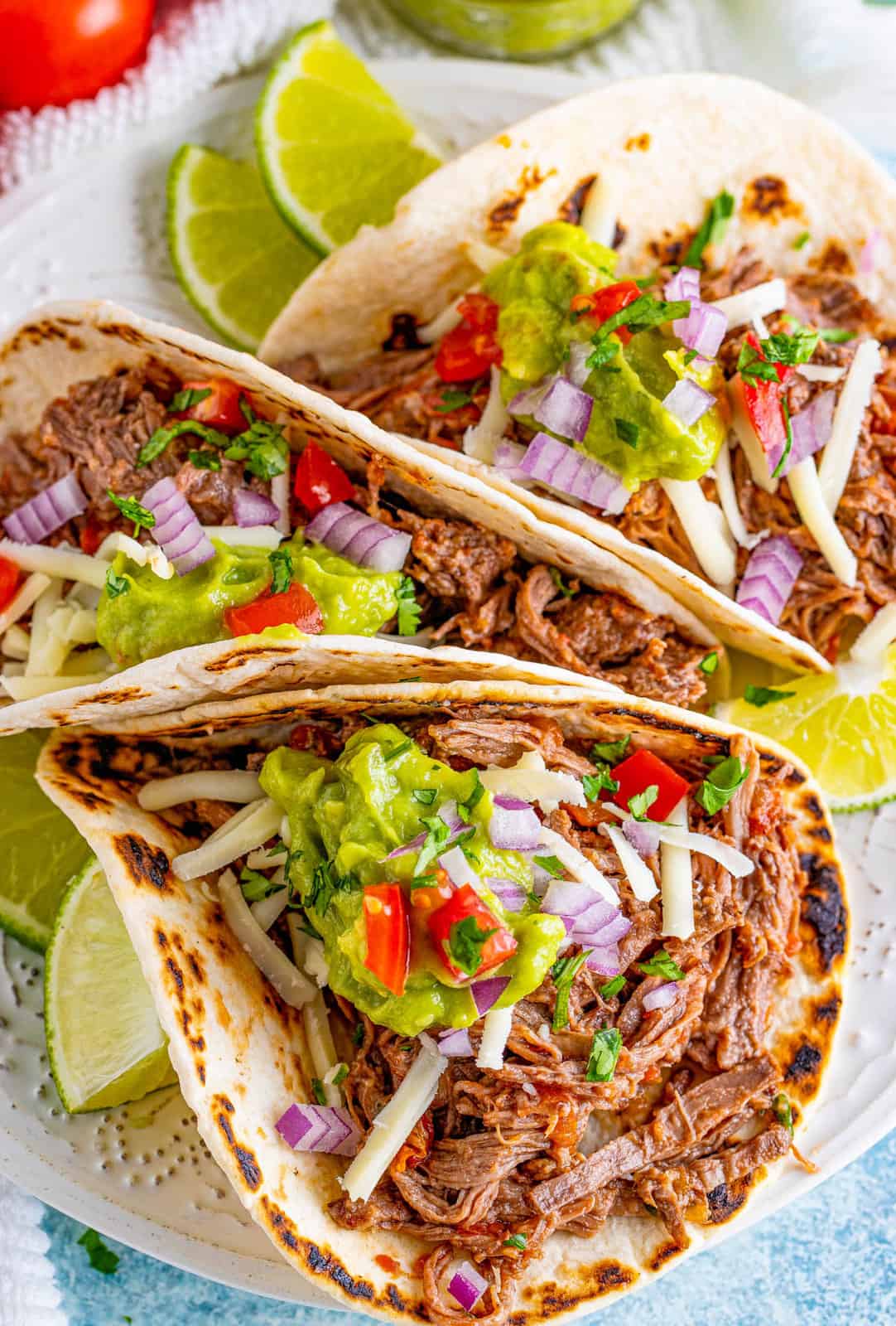 Overhead of three Slow Cooker Shredded Beef Tacos on plate with toppings.