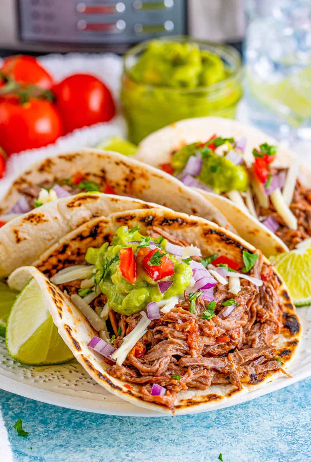 Slow Cooker Shredded Beef Tacos on plate with toppings and a lime.