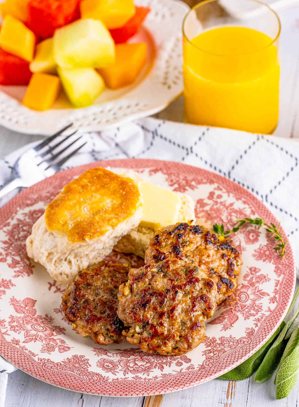 Four stacked patties of the Breakfast Sausage Recipe on plate with biscuit and butter.