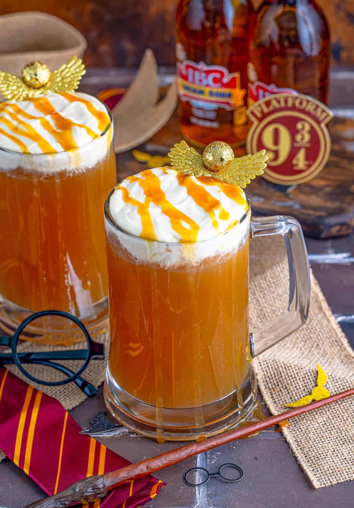 Two glasses of the Butterbeer Recipe with golden snitches and drizzle over topping.