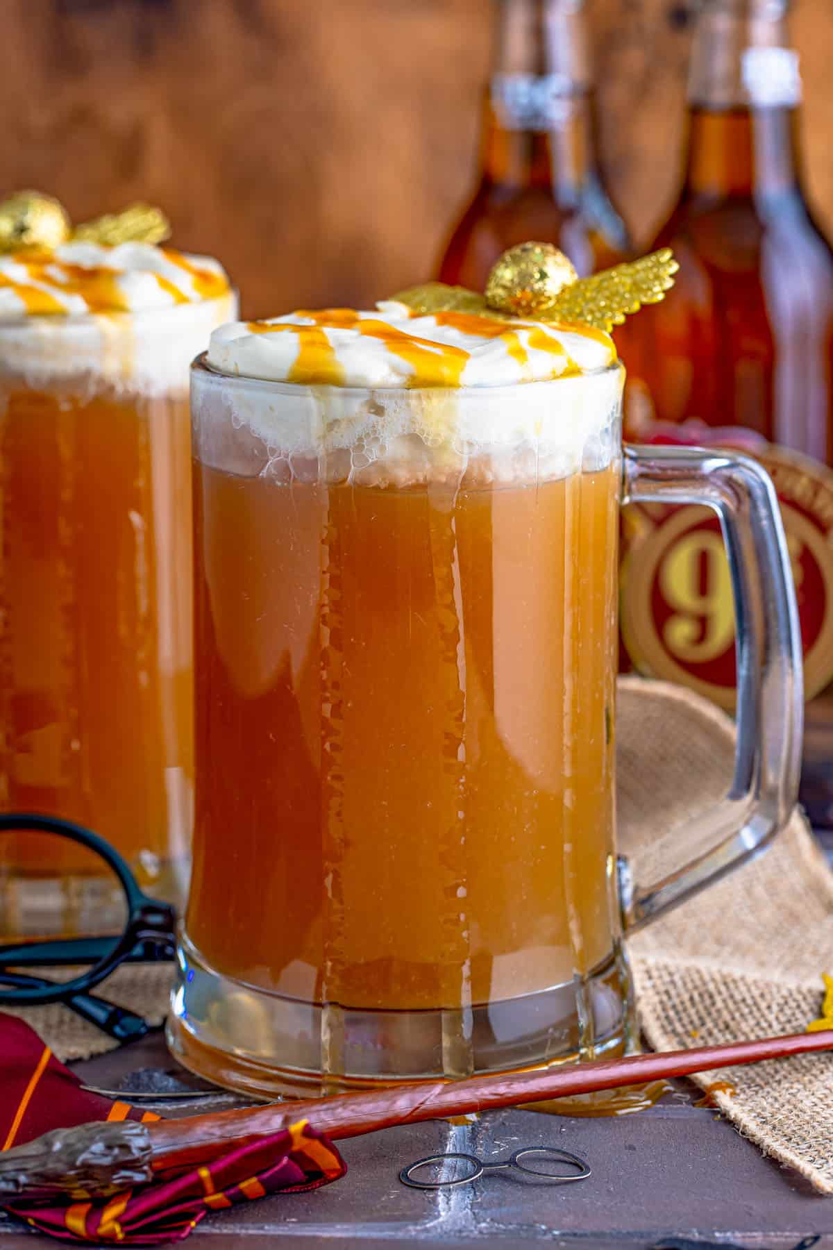Butterbeer Recipe in tall large handled mugs with whipped topping and butterscotch drizzle.