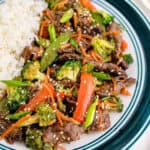 Square image of stir fry on plate next to rice.