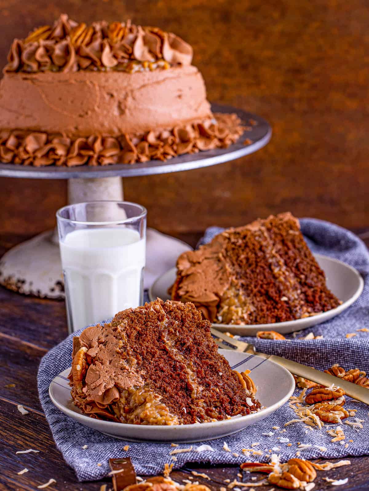 Two slices of the German Chocolate Cake Recipe on plates with cake on stand.