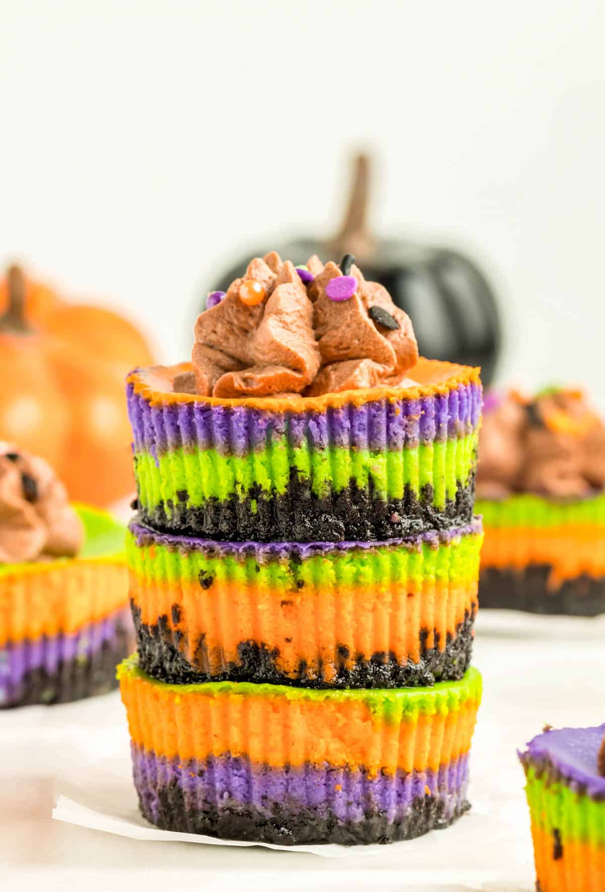 Three stacked Mini Halloween Cheesecakes with the top one topped with whipped cream and sprinkles.
