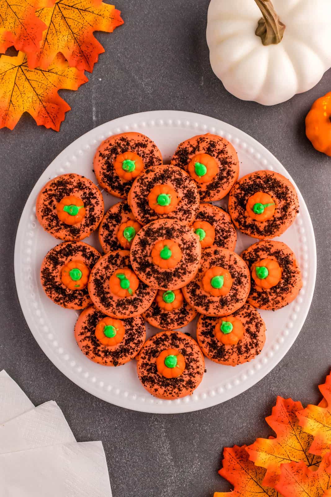 Overhead of stacked Pumpkin Patch Cookies on white plate with leave and pumpkins.
