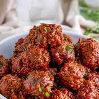 Stacked Slow Cooker Cranberry Meatballs in white bowl garnished with parsley.