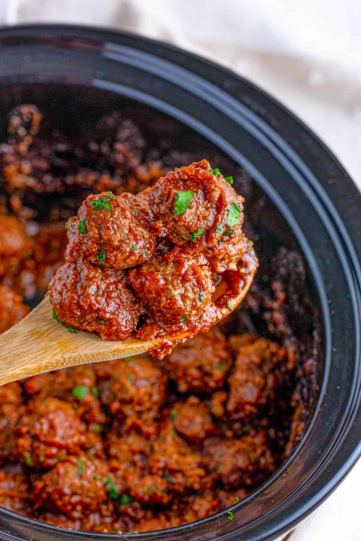 Spoon holding up Slow Cooker Cranberry Meatballs out of crock pot.
