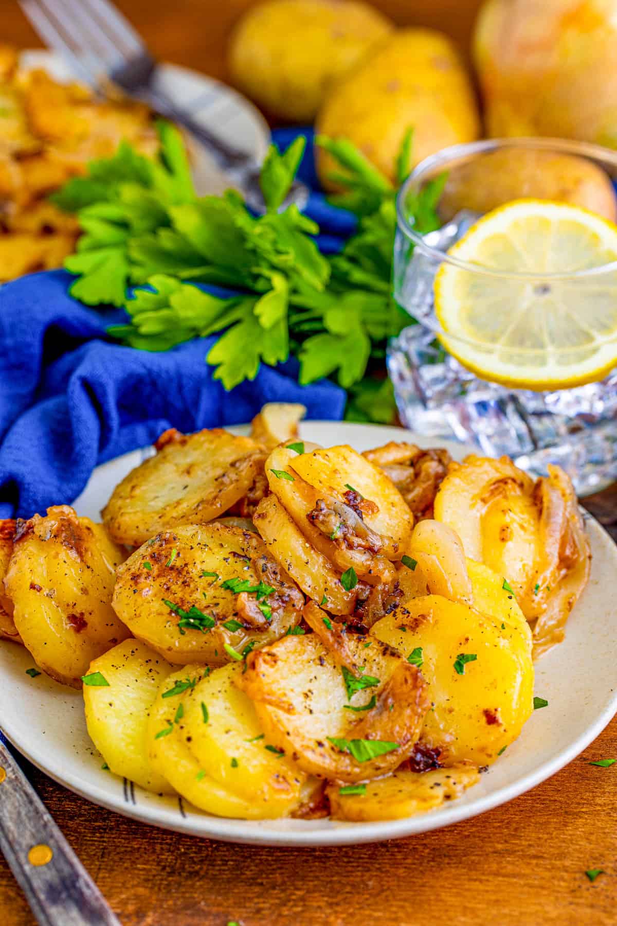 White plate with Smothered Potatoes on it with parsley and water in background.