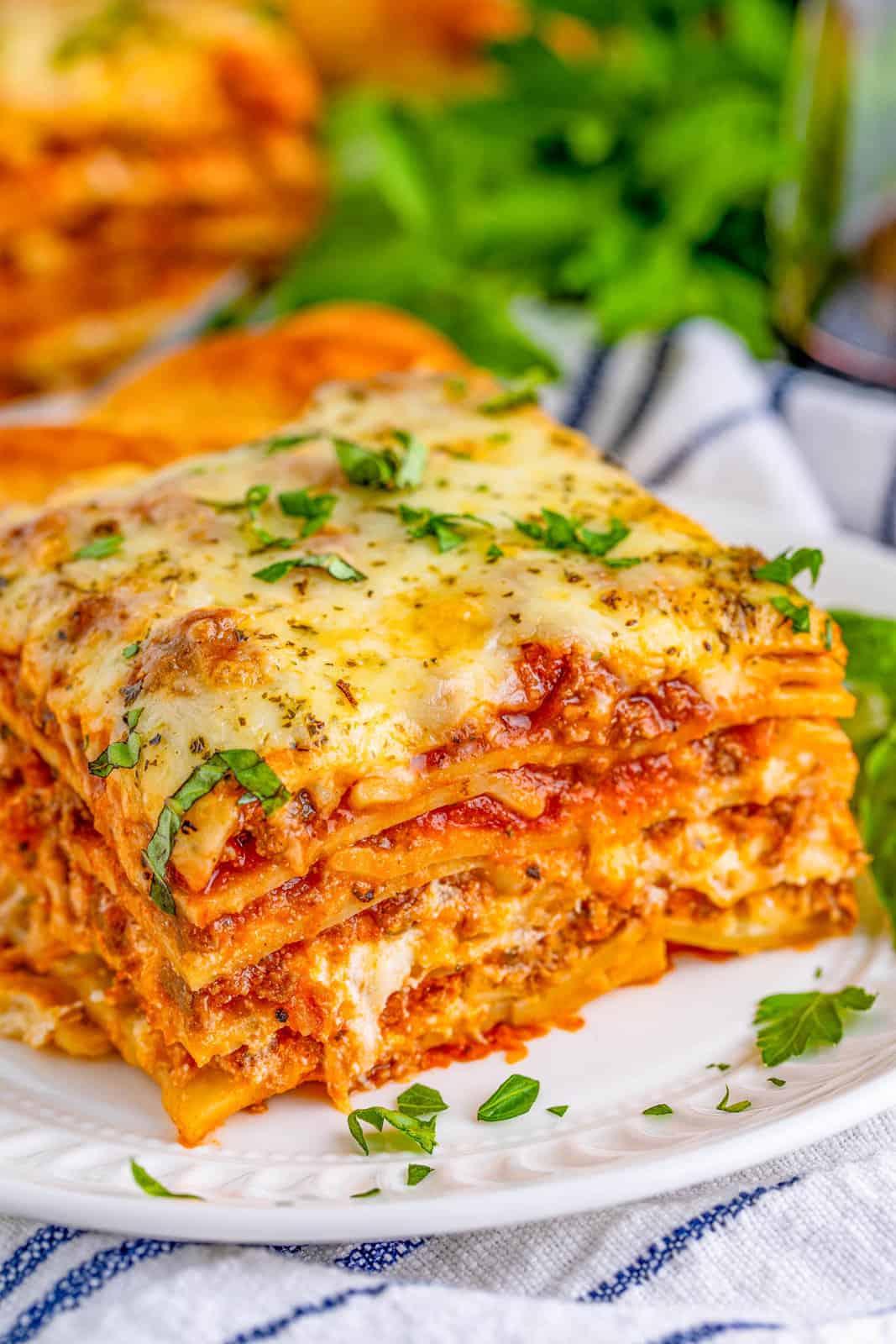 A slice of The Best Lasagna on white plate topped with herbs.