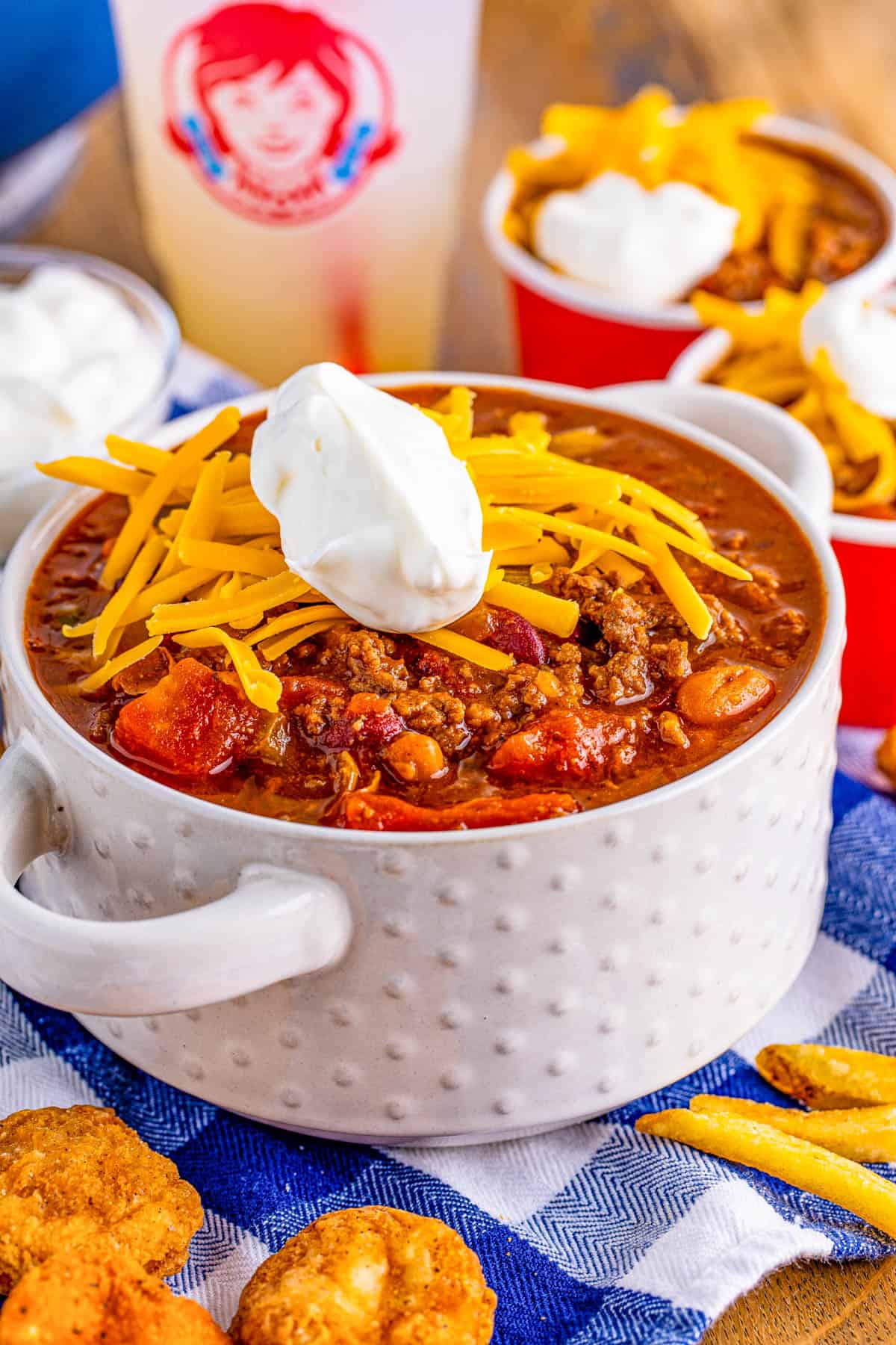Wendy's Chili in white bowl with handles topped with cheese and sour cream.
