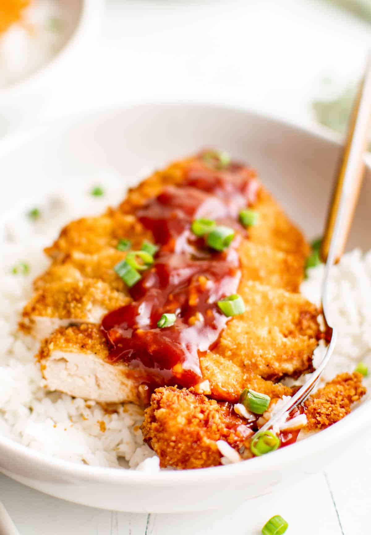 Bowl of rice with the Chicken Katsu Recipe on top with sauce and green onions.