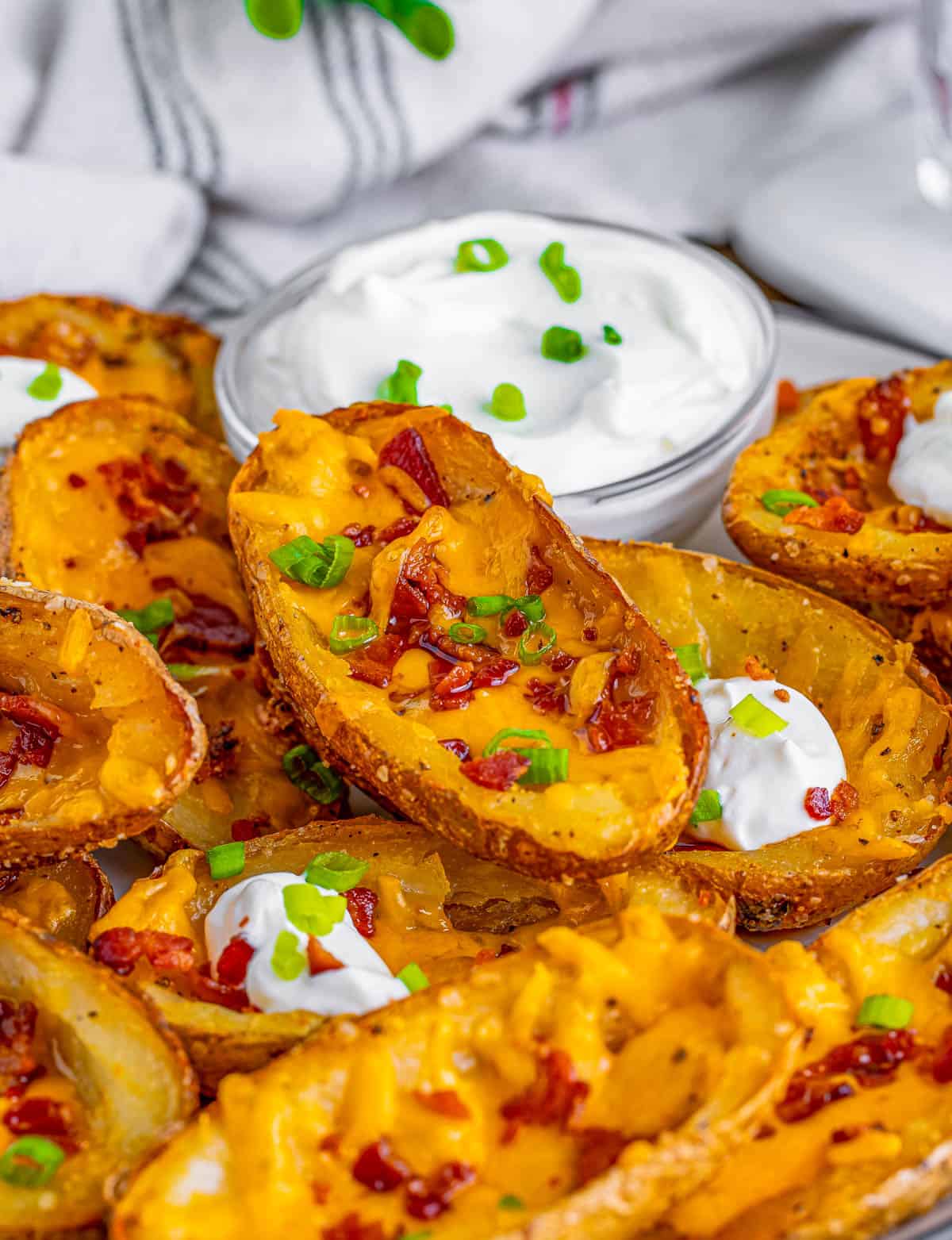Stacked Loaded Potato Skins on white plate with dipping sauce in back.