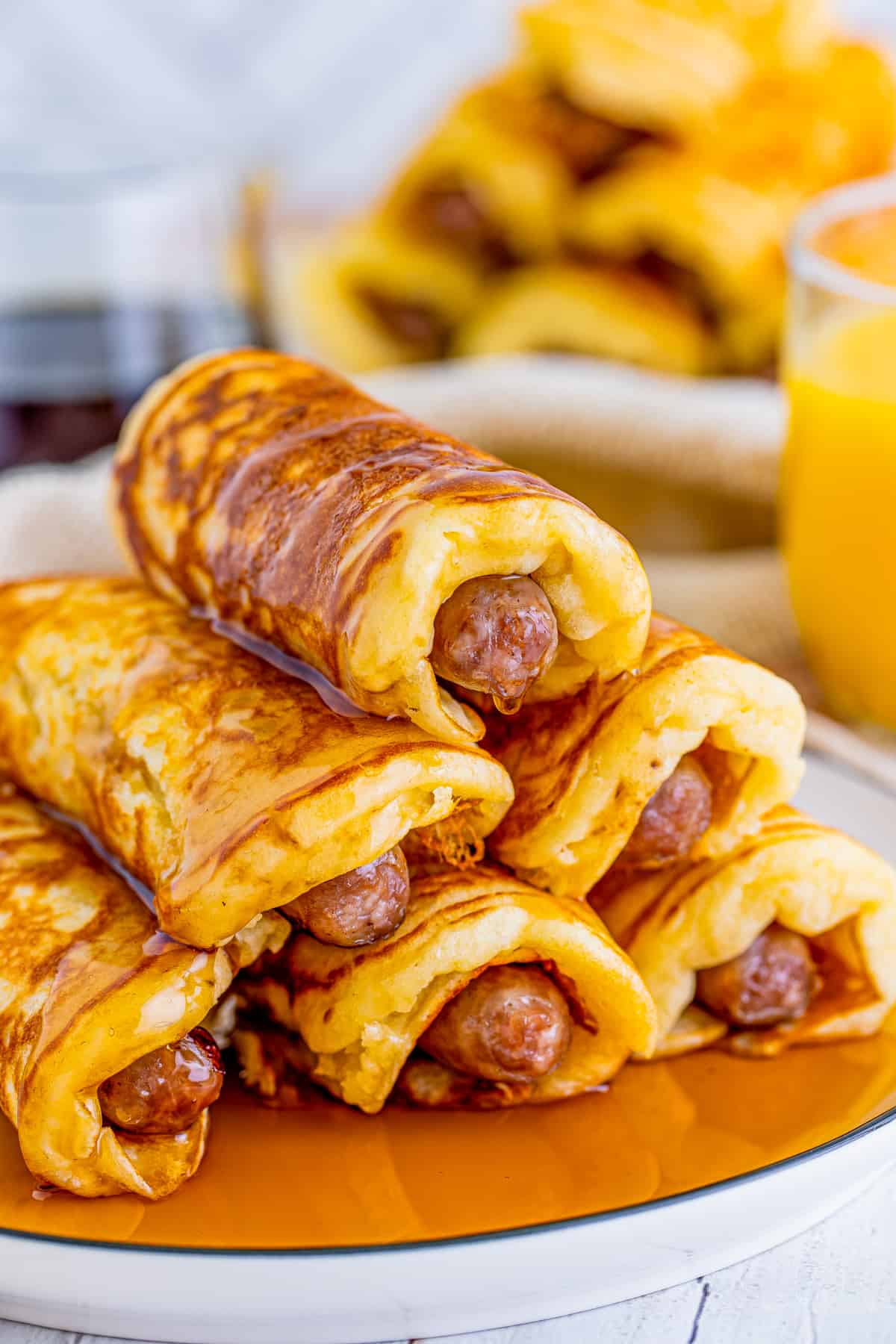 Stacked Breakfast Pigs in a Blanket on white plate with syrup on top.