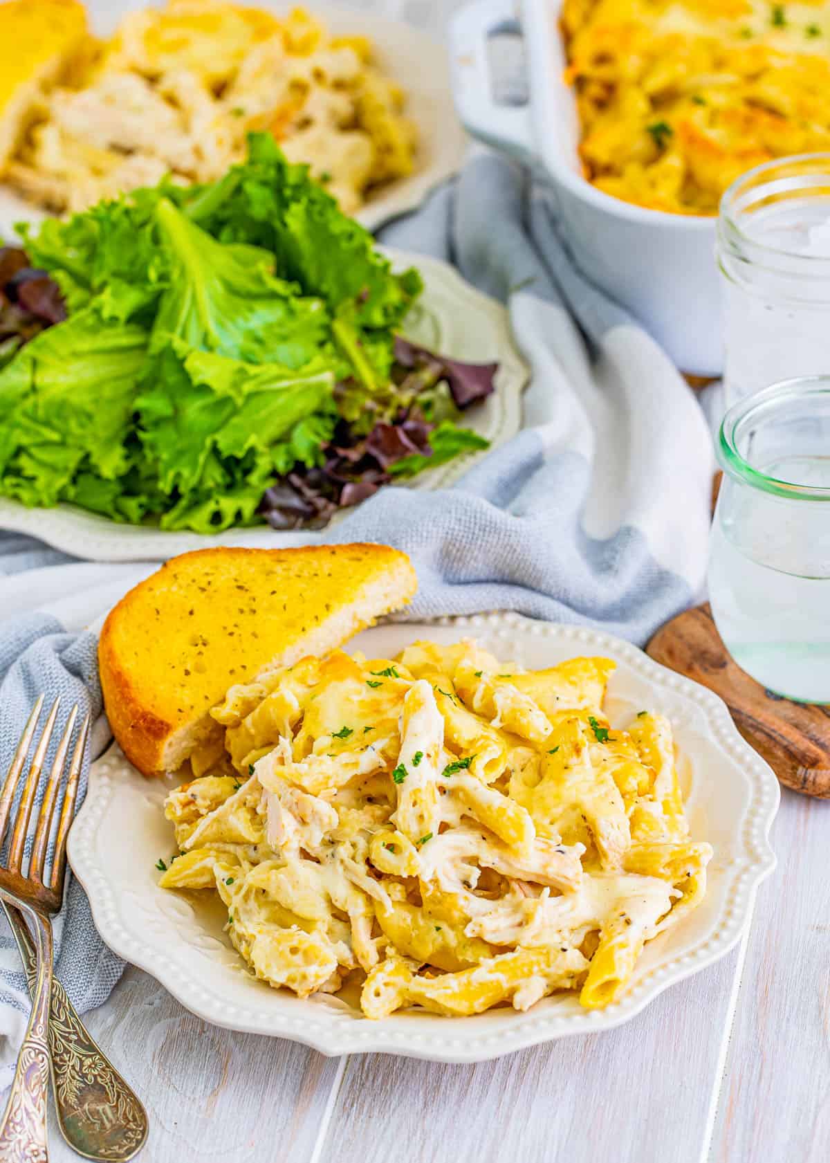 Chicken Alfredo Casserole on plate with bread and salad in background.
