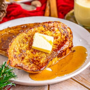 Close up square image of French Toast on plate with pat of butter and syrup.