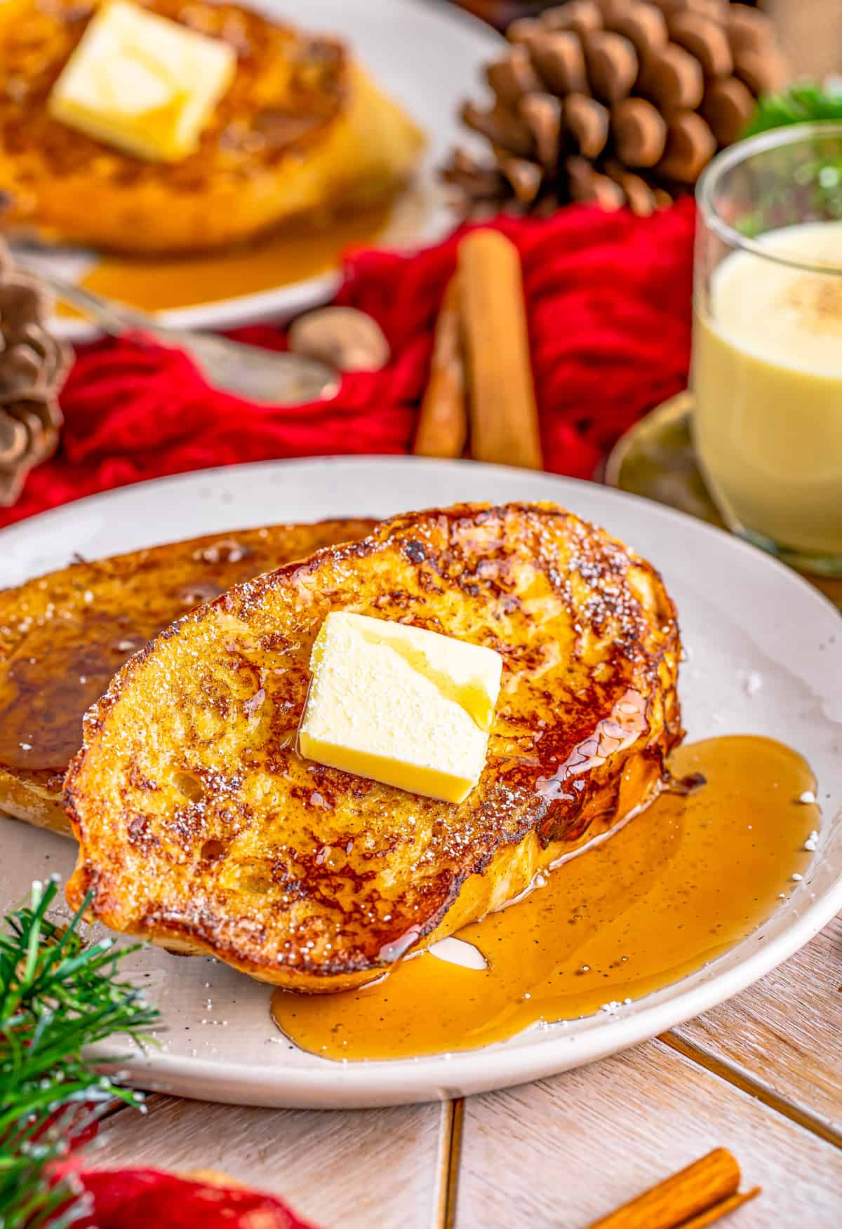 Two slices of Eggnog French Toast on plate with syrup and butter.