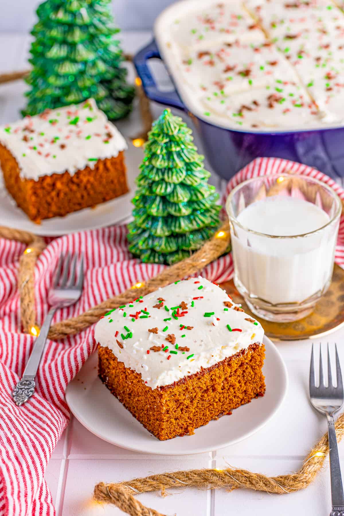 Two slices of Gingerbread Cake on white plate with milk and fake christmas trees.