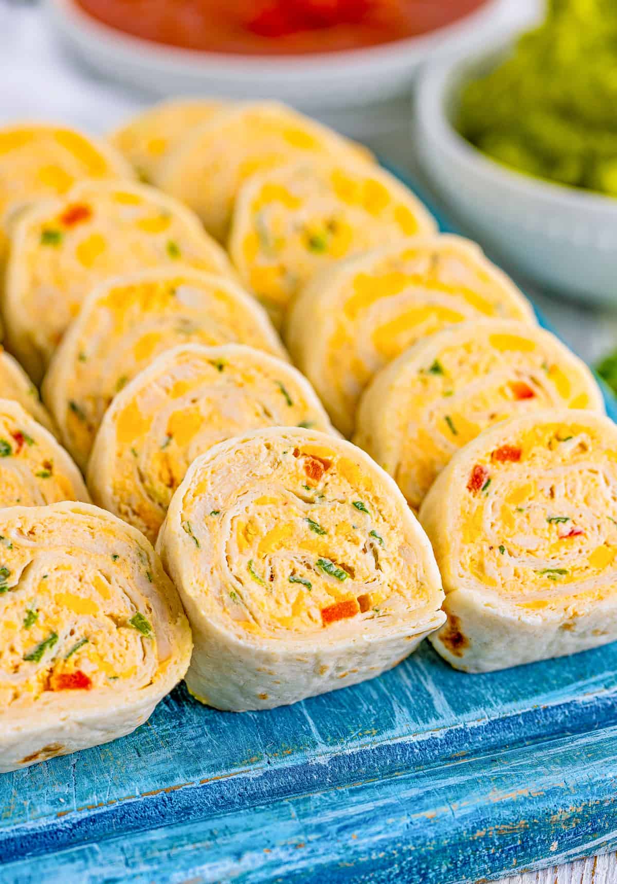 Close up of lined up Mexican Pinwheels on blue wooden board showing filling.