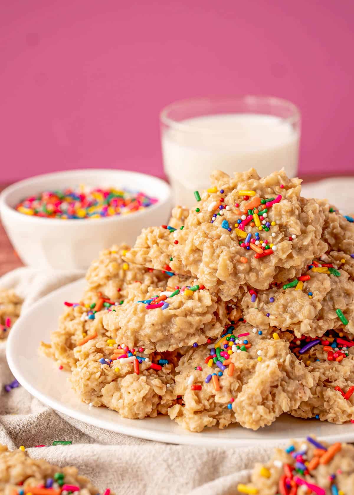 Vanilla No Bake Cookies stacked on white plate with milk and sprinkles in background.
