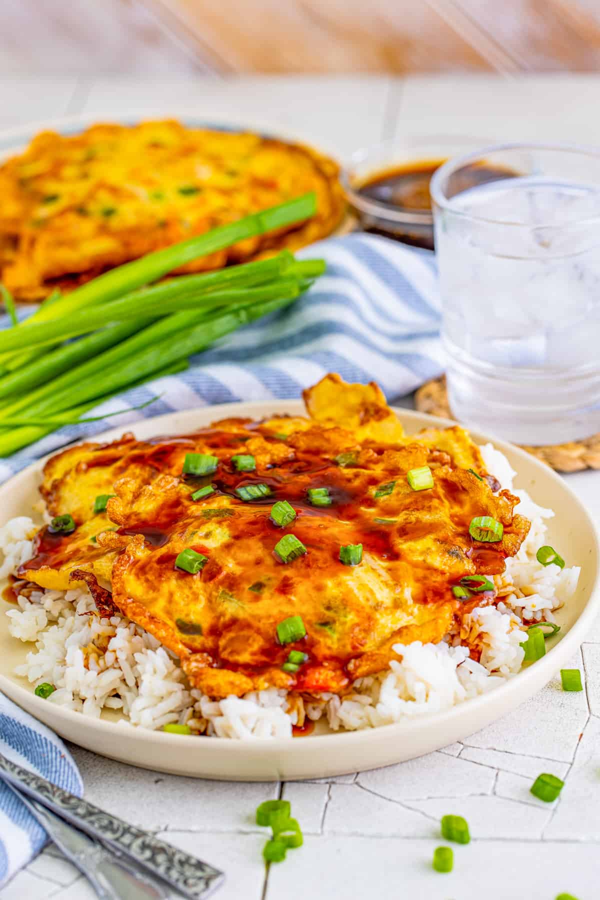 Vegetable Egg Foo Young over rice on plate with sauce on top.