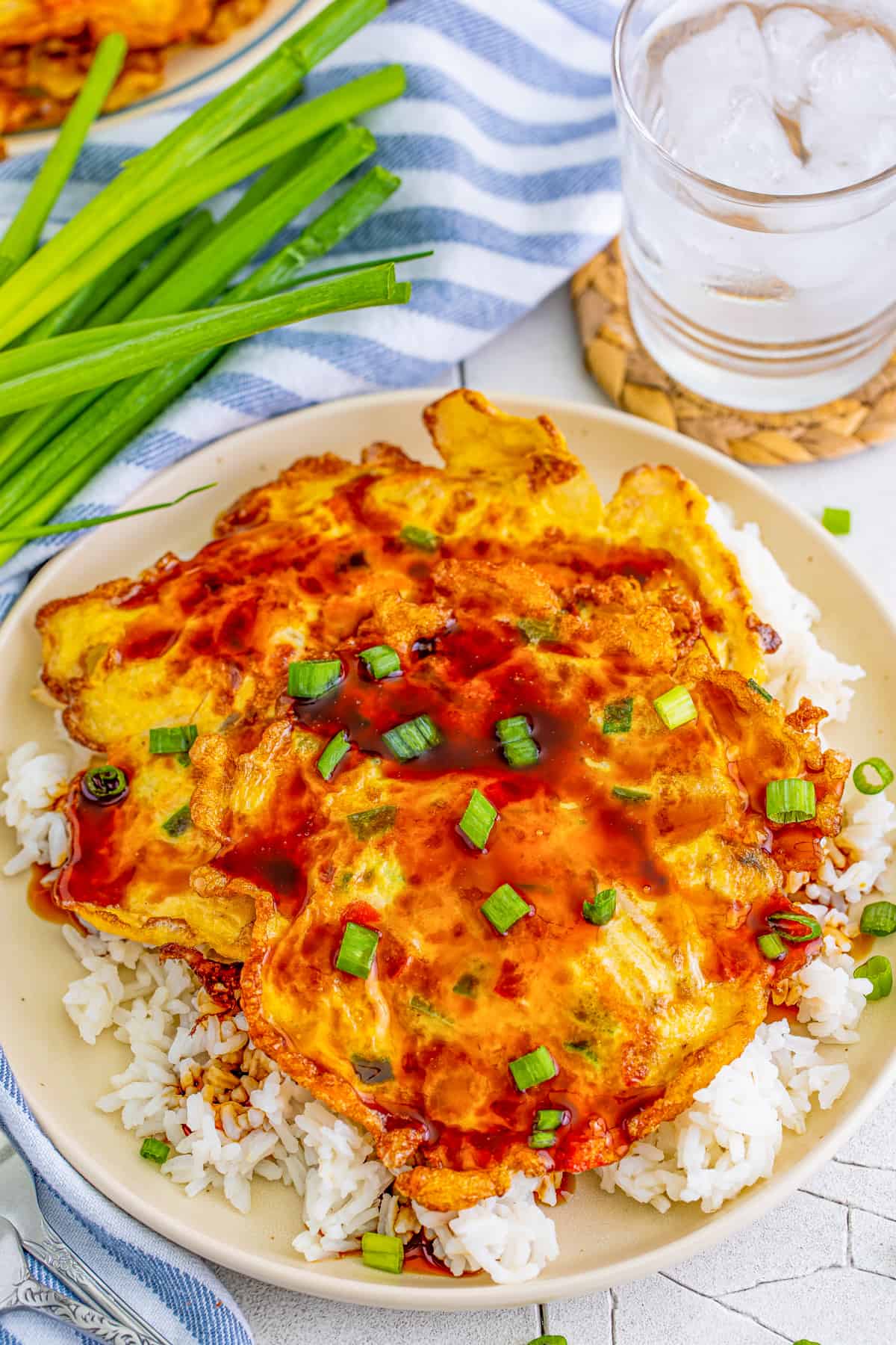 Overhead of one Egg Foo Young over rice with sauce and green onions.