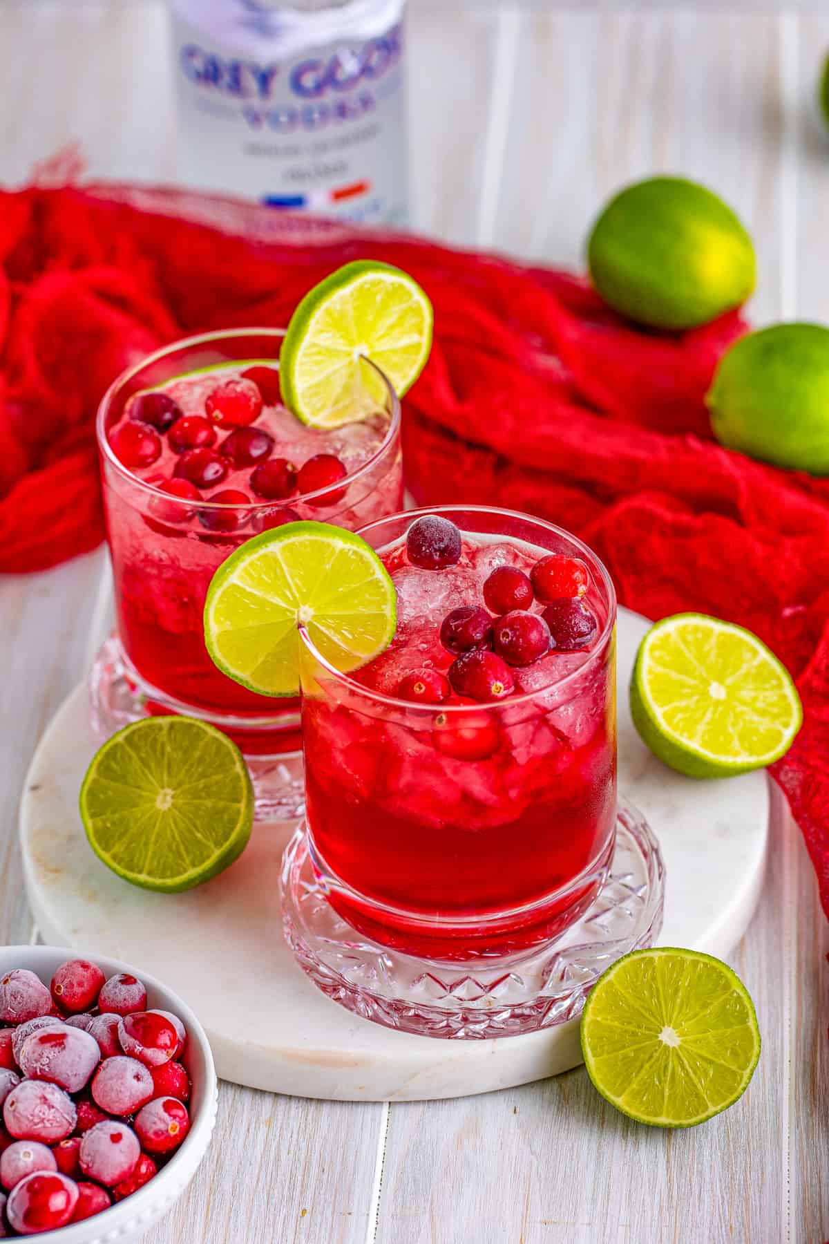 Vodka Cranberry in glasses on white platter with garnishes.