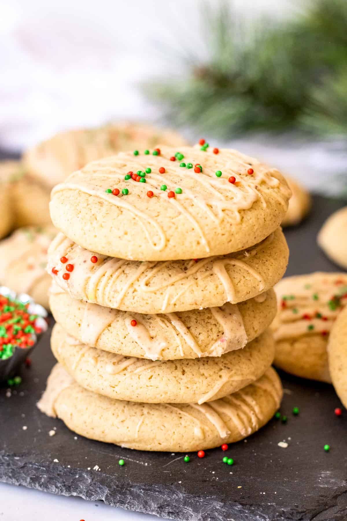 Five stacked Eggnog Cookies on slate with glaze and sprinkles.