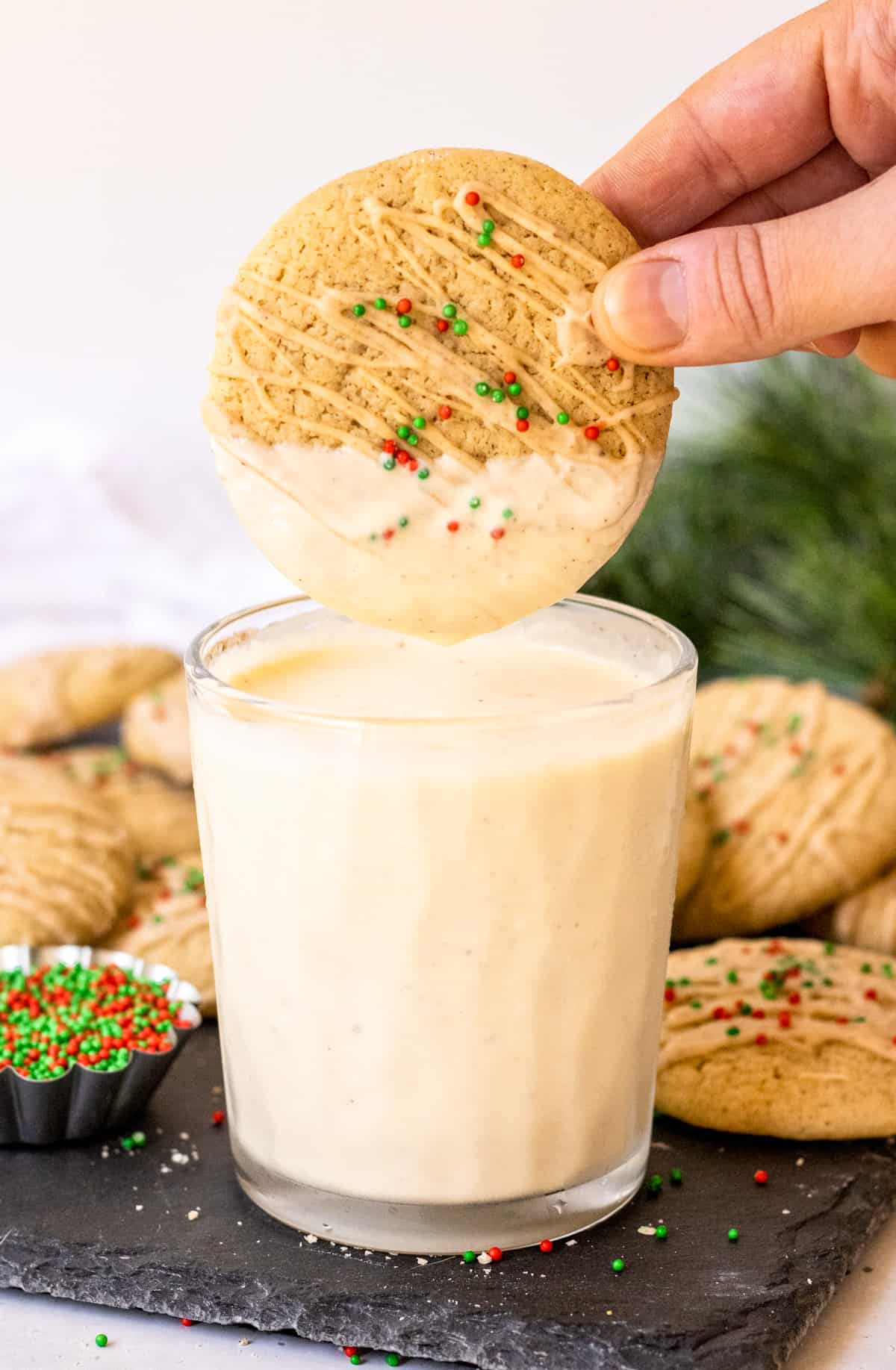 Hand dipping one cookie in eggnog.