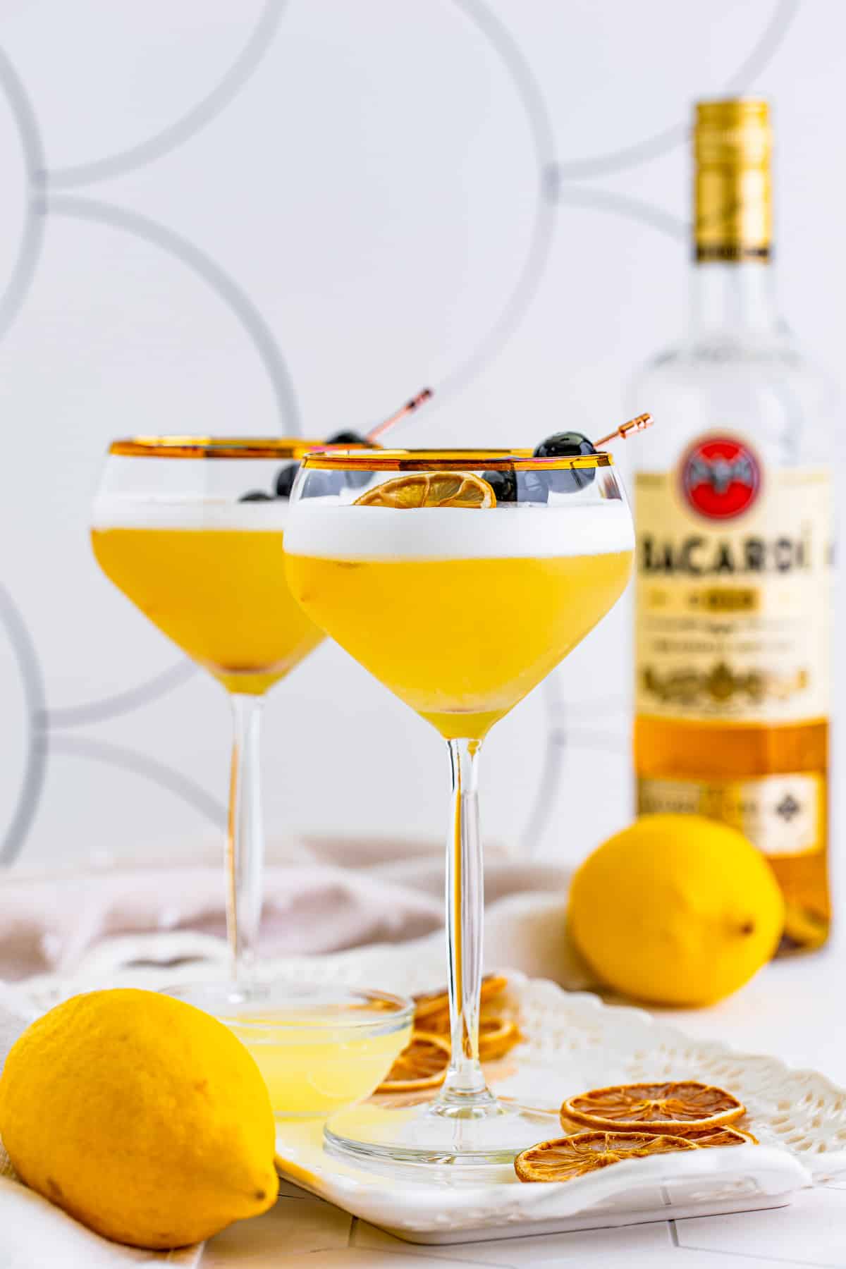 Rum Sour in two glasses with alcohol in background and oranges around platter.