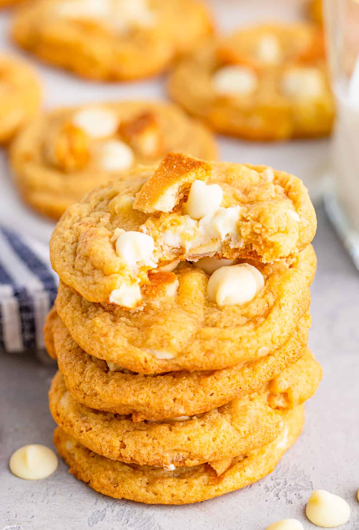 Stacked Banana Pudding cookies with a bite taken out of the top cookie showing the white chocolate chips.