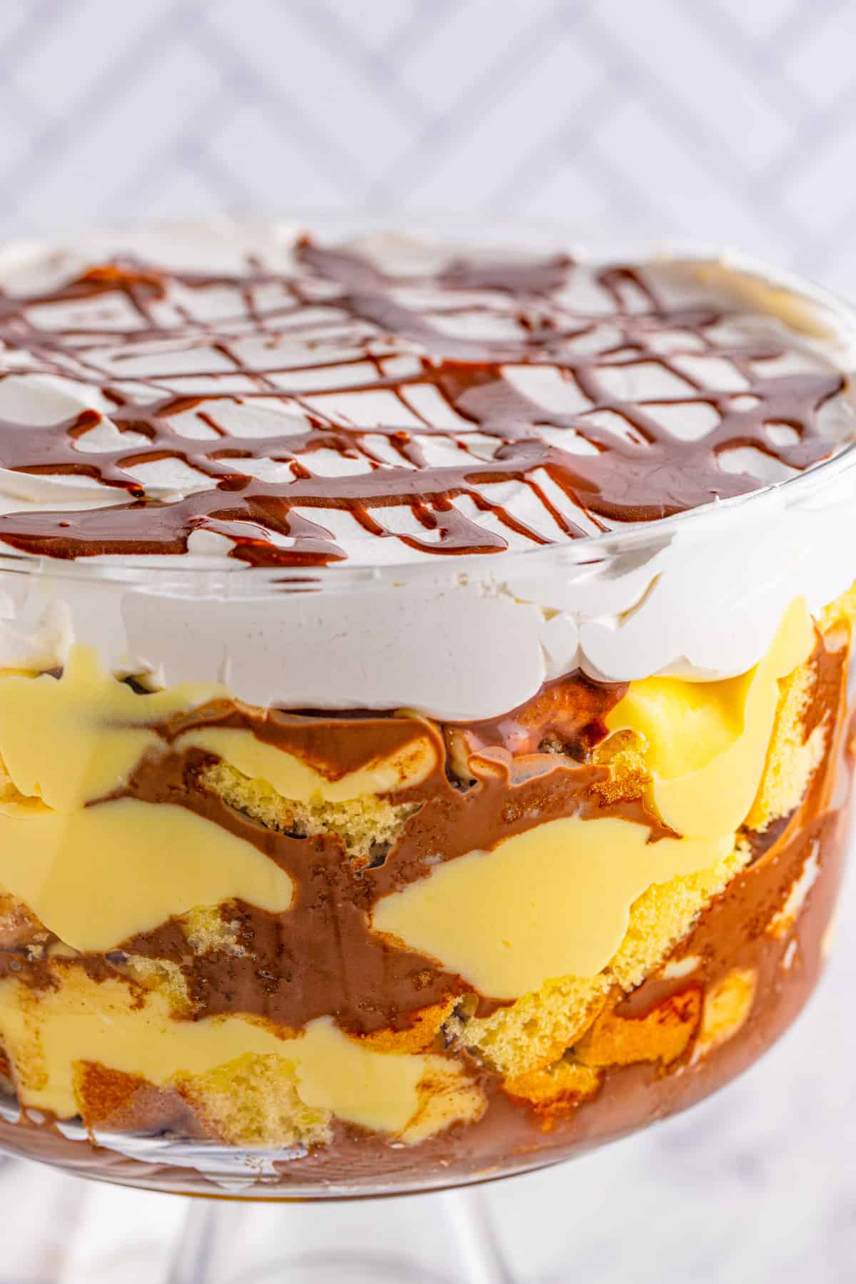 Close up of finished trifle in trifle bowl showing layers of cake, pudding and chocolate topped with whipped topping.