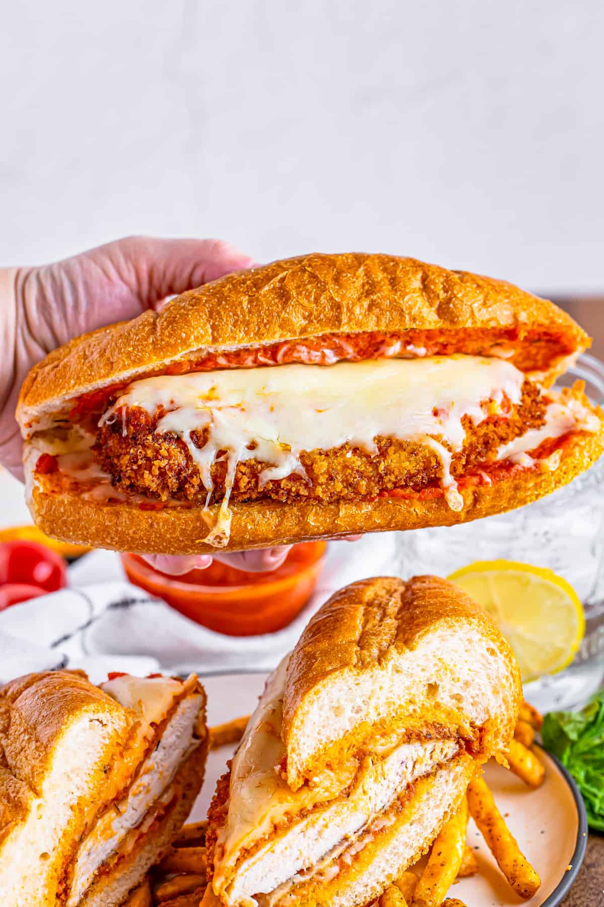 Hand holding up one of the Chicken Parmesan Sandwiches.