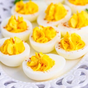 Close up square image of finished eggs topped with paprika on white platter.