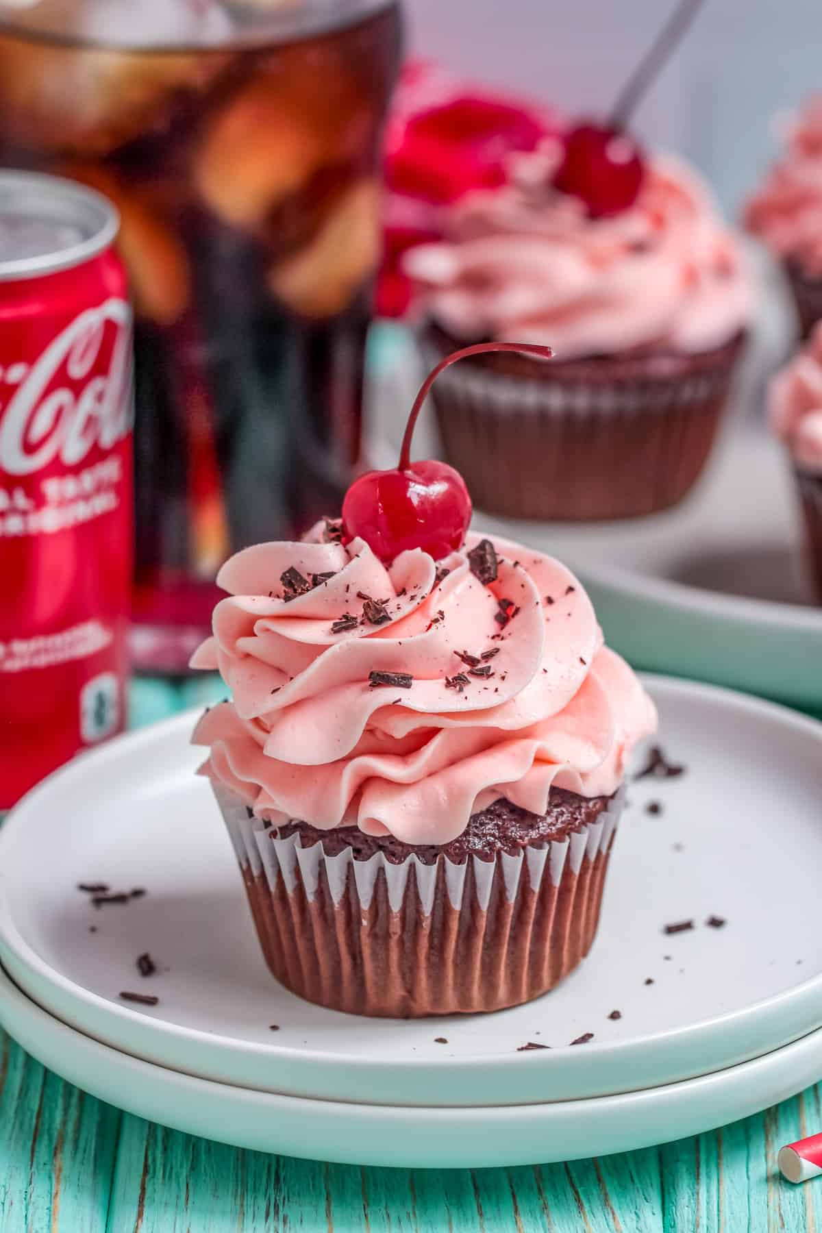 One of the Cherry Coke Cupcakes on white plate frosted and garnished with a cherry and chocolate shavings.