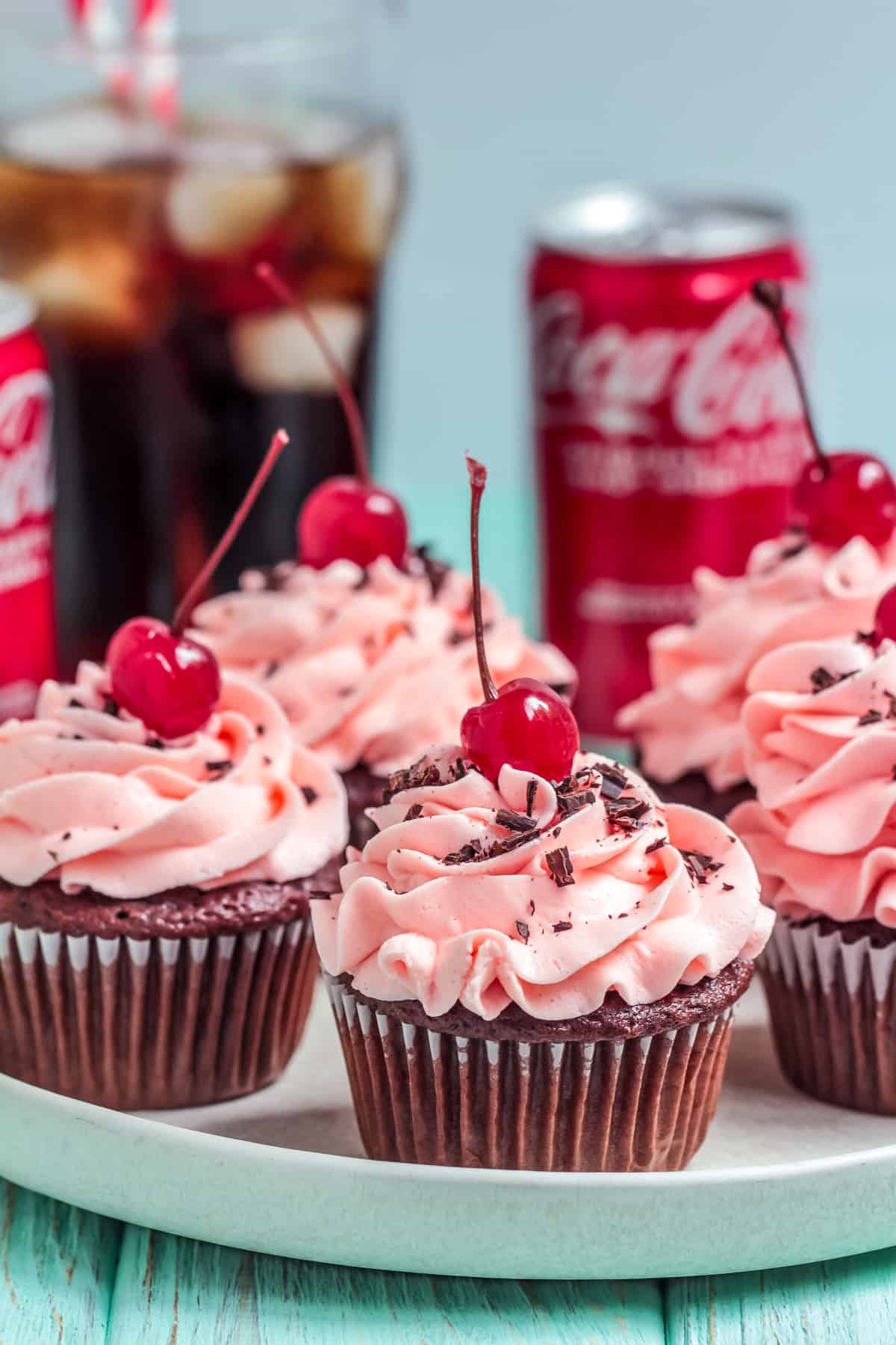 Multiple Cherry Coke Cupcakes on platter garnished with coke can and glass in background.
