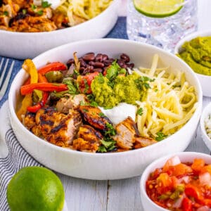 Square image of finished Burrito Bowls with lime, pico and guacamole around bowl.