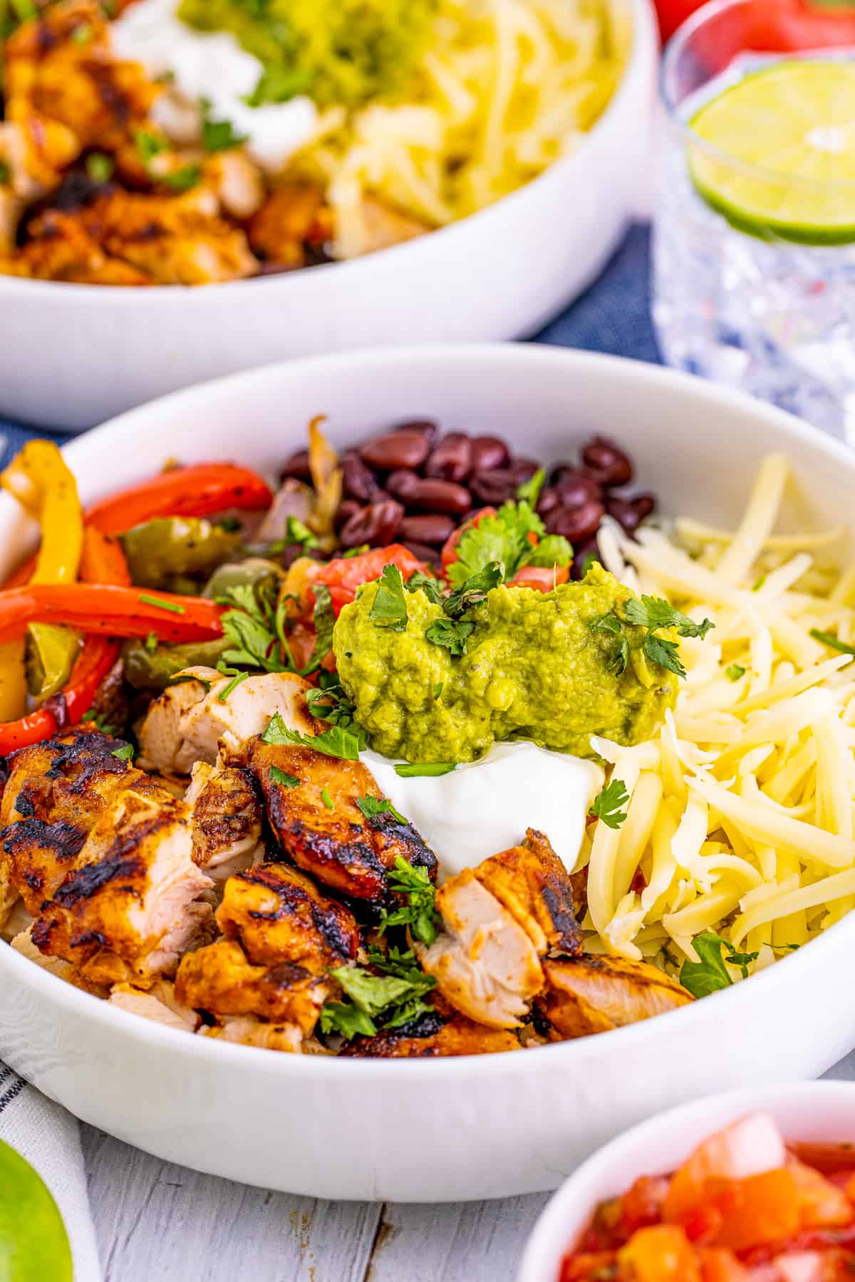 Close up of one of the Chicken Burrito Bowls and the ingredients in white bowl.