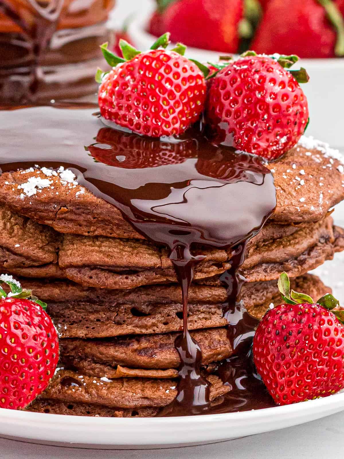 Close up of stacked Chocolate Pancakes on plate showing the chocolate sauce drizzling down the side.