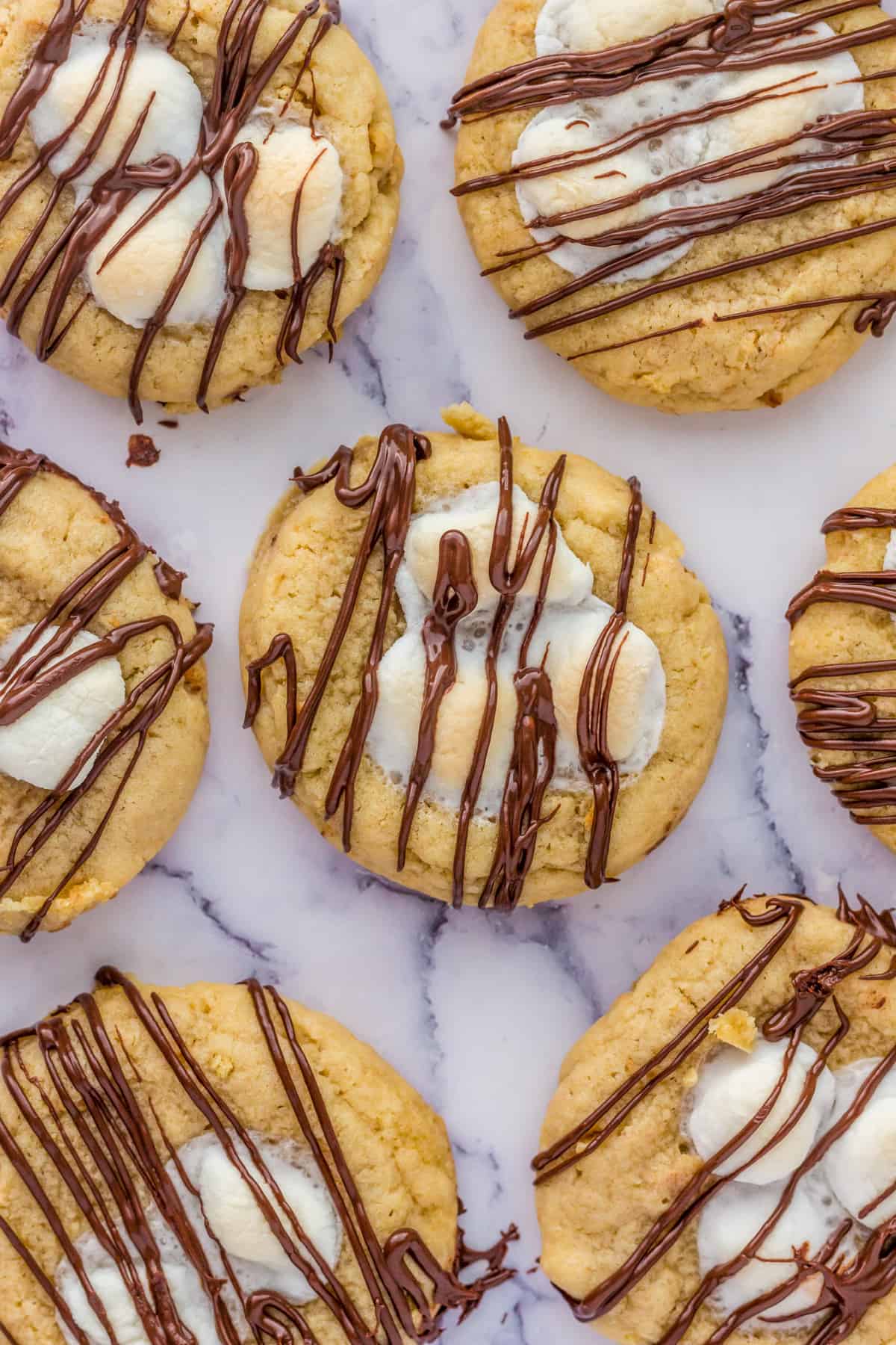 Finished S'mores Thumbprint Cookies on marble board with melted marshmallows and chocolate.