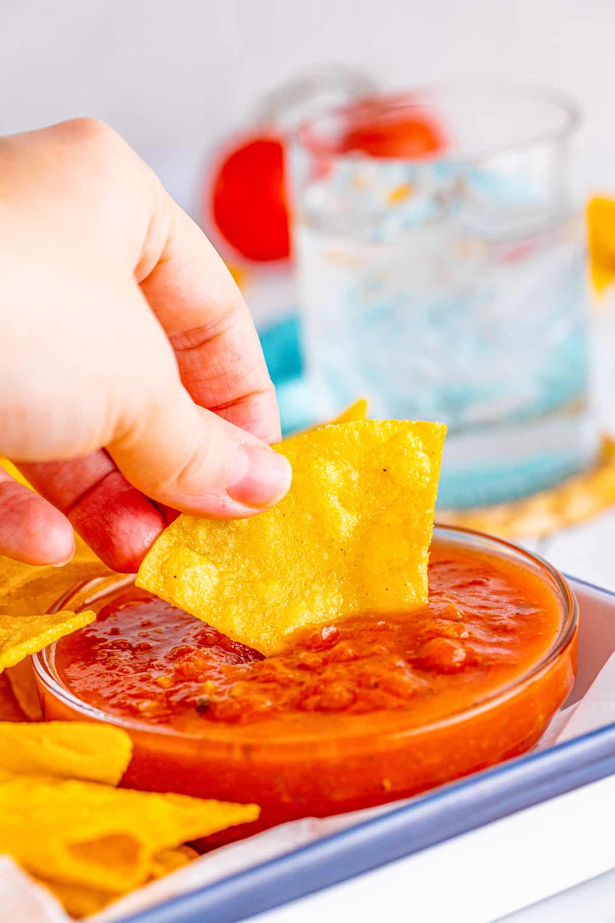 Hand dipping one chip into salsa in a bowl.
