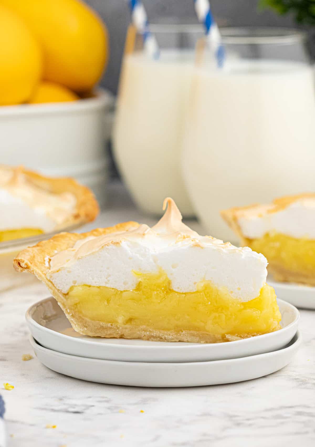Slice of the Lemon Meringue Pie Recipe on two white plates with milk in background.