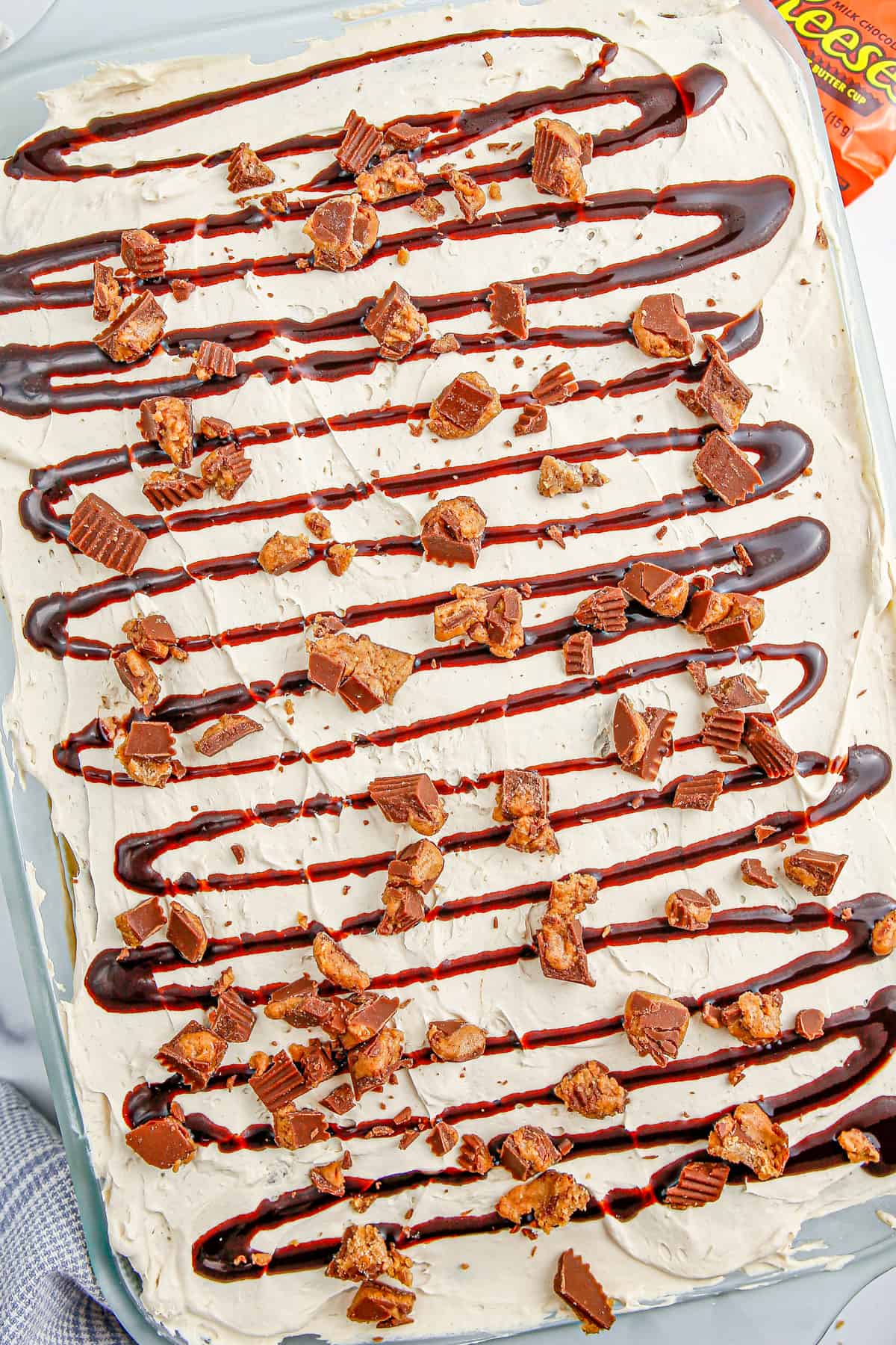 Overhead photo of finished Reese's Ice Cream Sandwich Cake topped with chopped Reese's and chocolate syrup.