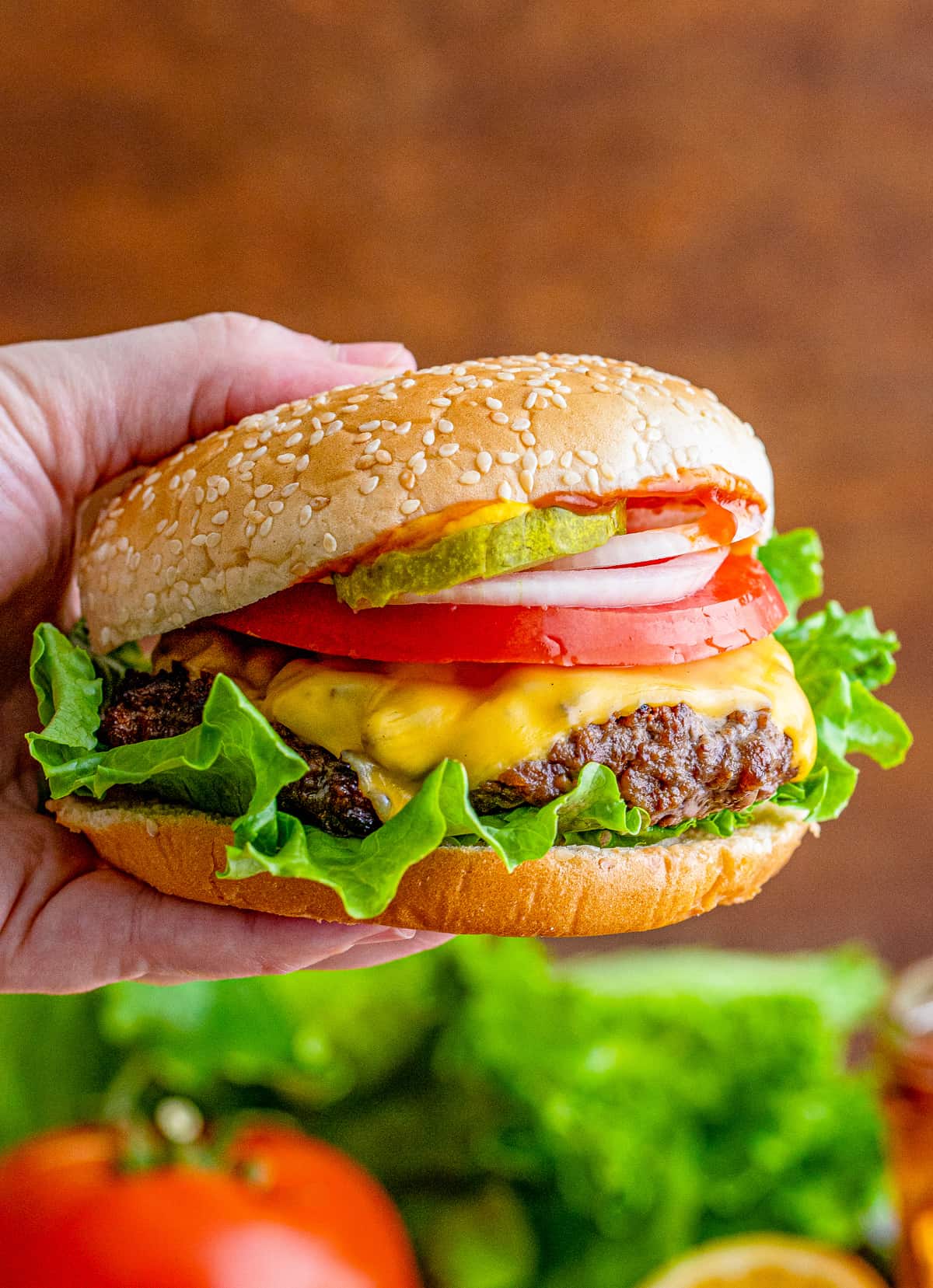 Hand holding up garnished cheeseburger, showing melted cheese down the side.