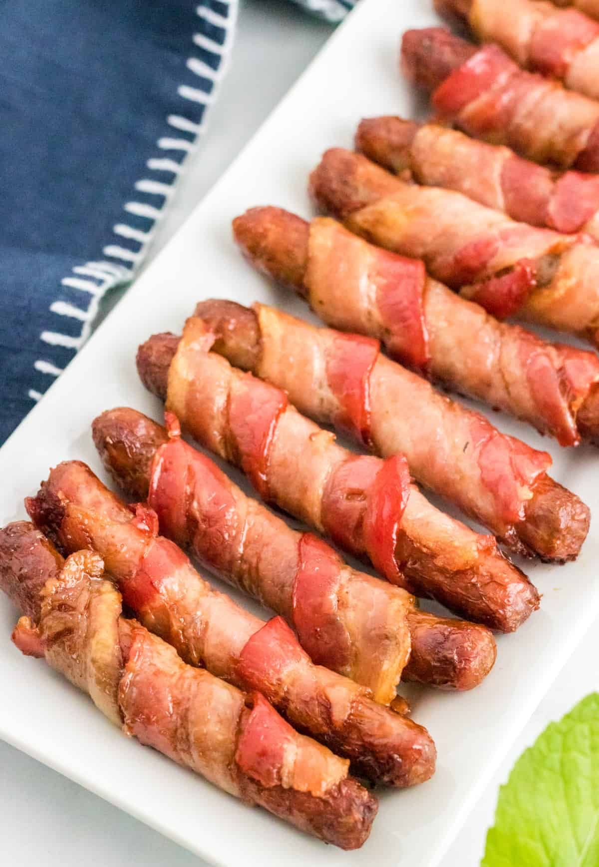 Overhead of Bacon Wrapped Sausages on white serving platter.
