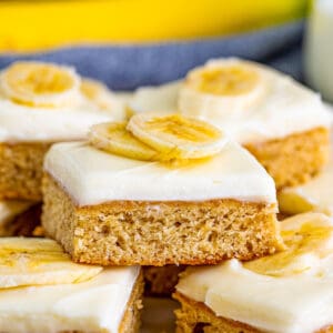 Close up square image of stacked blondies frosted with sliced of banana on them.