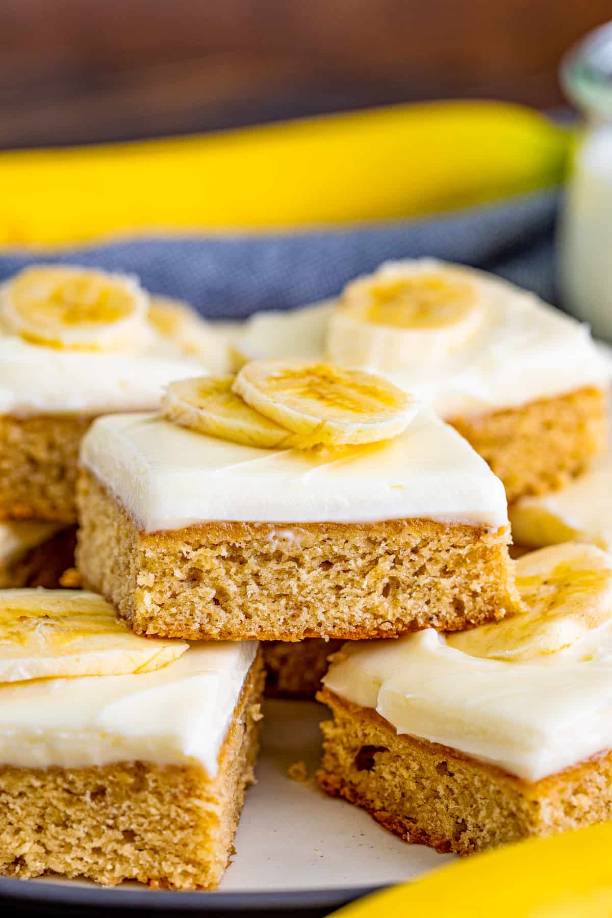 Stacked Banana Blondies on white plate with cream cheese frosting and sliced bananas on top.