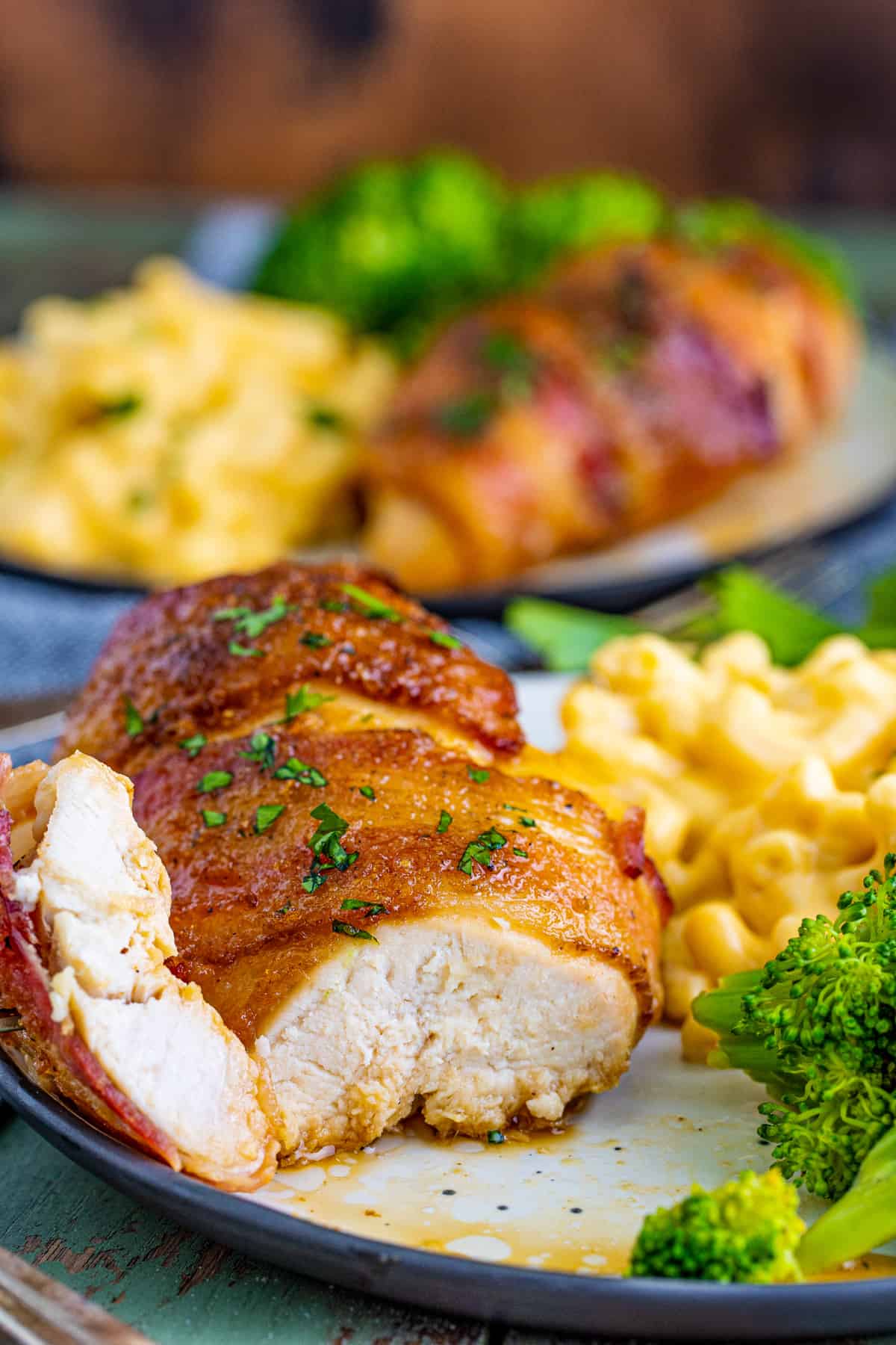 One piece of chicken on plate with a slice cut out showing the inside with mac and cheese and broccoli beside it.