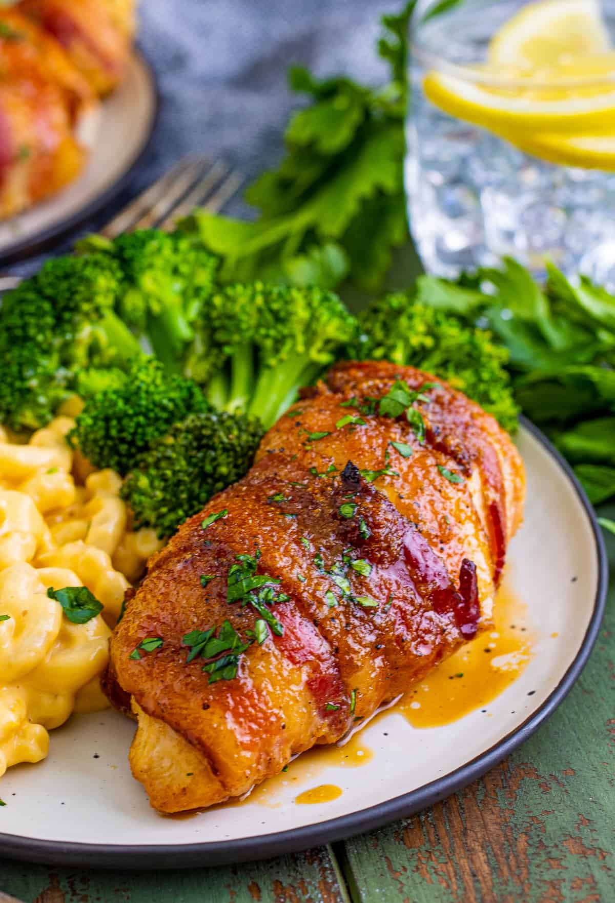 Bacon Wrapped Chicken on white plate garnished with parsley and served with macaroni and cheese and broccoli.