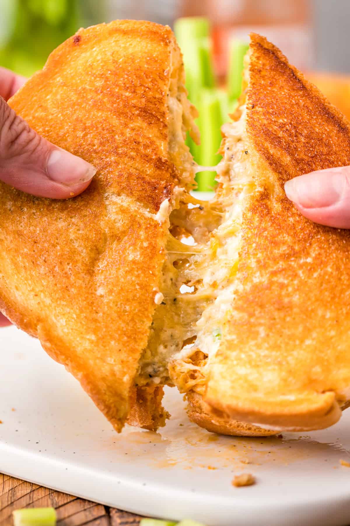 Hands pulling the Buffalo Chicken Grilled Cheese apart showing a slight cheese pull.